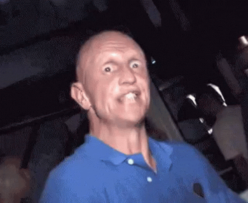 A Bald Man In A Blue Shirt Is Making A Funny Face . GIF