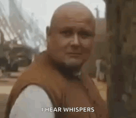 A Bald Man In A Brown Vest Is Standing In Front Of A Tree And Says `` I Hear Whispers '' . GIF