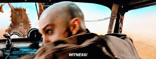 A Bald Man In A Car With The Word Witness Written On His Back GIF