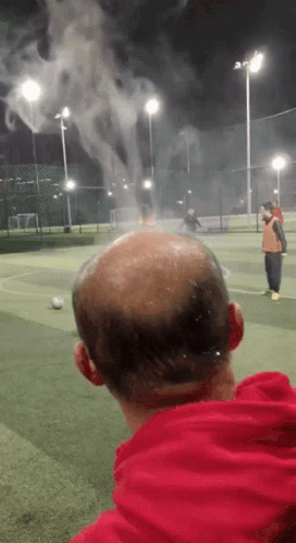 A Bald Man In A Red Hoodie Is Watching A Soccer Game GIF