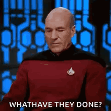 A Bald Man In A Red Shirt Is Sitting In Front Of A Blue Wall And Asking What Have They Done . GIF