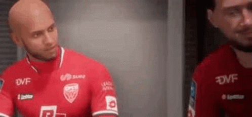 a bald man in a red soccer jersey is standing next to another bald man in a red jersey .