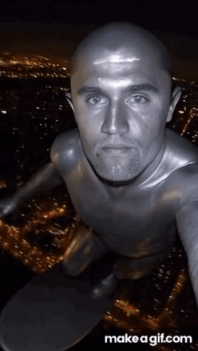 A Bald Man In A Silver Bodysuit Is Taking A Selfie GIF