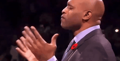 A Bald Man In A Suit And Tie Is Clapping His Hands In The Air . GIF