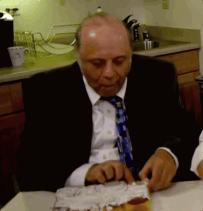 A Bald Man In A Suit And Tie Is Cutting A Piece Of Cake GIF