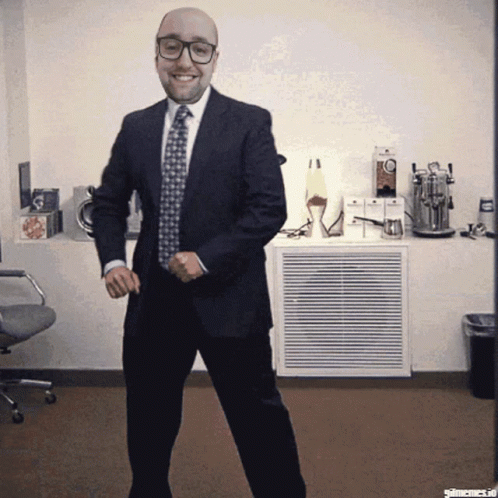 A Bald Man In A Suit And Tie Is Dancing In A Room GIF