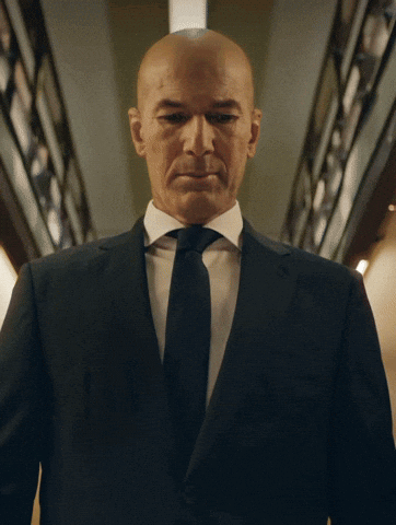 A Bald Man In A Suit And Tie Is Looking At The Camera GIF