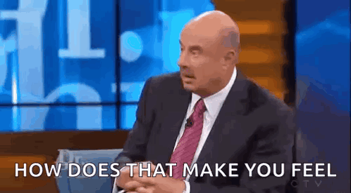 A Bald Man In A Suit And Tie Is Sitting On A Stage And Talking To Someone . GIF