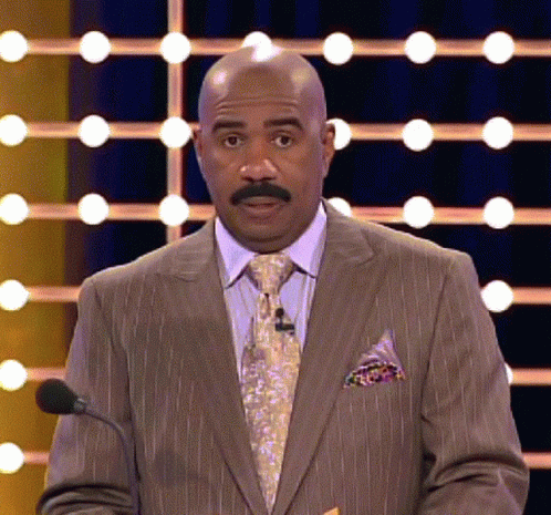A Bald Man In A Suit And Tie Is Speaking Into A Microphone GIF
