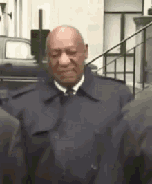 a bald man in a suit and tie is standing next to a group of people .