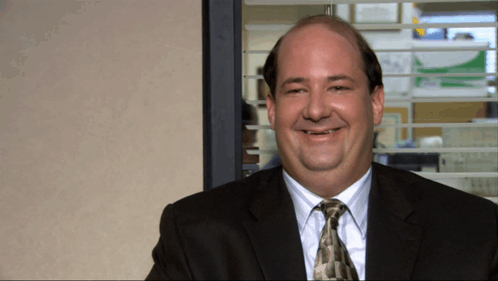 A Bald Man In A Suit And Tie Smiles In Front Of A Window GIF