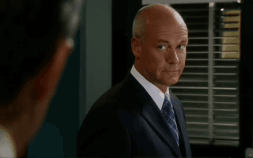 A Bald Man In A Suit And Tie Stands In Front Of A Screen That Says Get Over It GIF