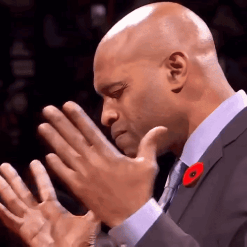 A Bald Man In A Suit And Tie With A Poppy On His Lapel GIF
