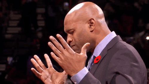 A Bald Man In A Suit And Tie With A Poppy Pin On His Lapel GIF