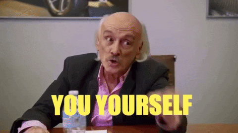 A Bald Man In A Suit Is Sitting At A Table With The Words `` You Yourself '' Written In Yellow . GIF