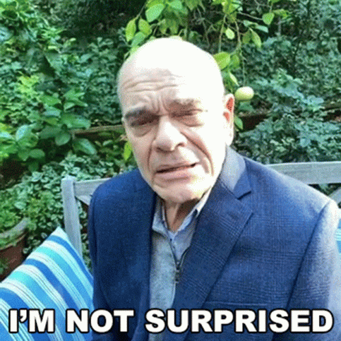 A Bald Man In A Suit Is Sitting On A Bench With The Words I 'M Not Surprised Above Him GIF