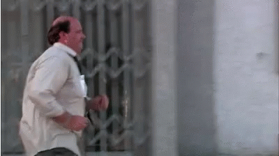 a bald man in a white shirt and tie is running across a street .