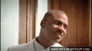 A Bald Man In A White Shirt Is Smiling In Front Of A Door . GIF