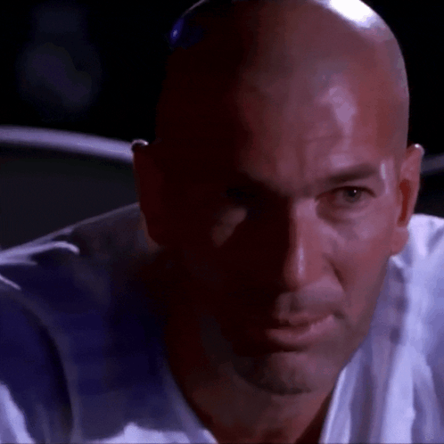 A Bald Man In A White Shirt Looks At The Camera GIF