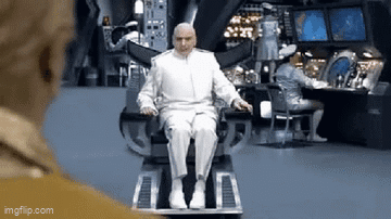 A Bald Man In A White Suit Is Sitting In A Chair In A Room . GIF