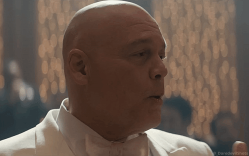 A Bald Man In A White Tuxedo And Bow Tie Is Talking GIF