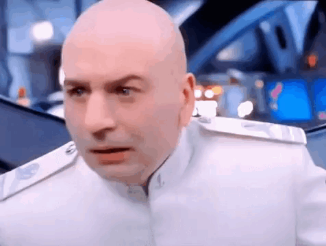 A Bald Man In A White Uniform Is Making A Funny Face And Looking At The Camera . GIF