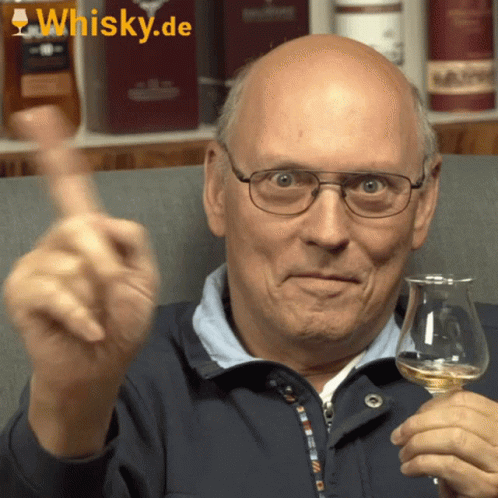 A Bald Man Is Holding A Glass Of Whisky And Giving A Thumbs Up Sign GIF