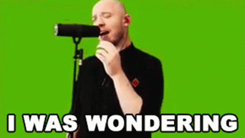A Bald Man Is Singing Into A Microphone With The Words `` I Was Wondering '' Written On The Screen Behind Him . GIF