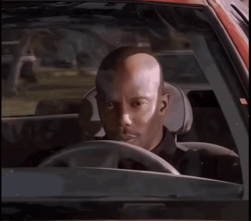 A Bald Man Is Sitting In The Driver 'S Seat Of A Car Looking At The Camera . GIF