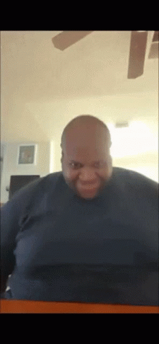 A Bald Man Is Smiling In Front Of A Ceiling Fan In A Living Room GIF