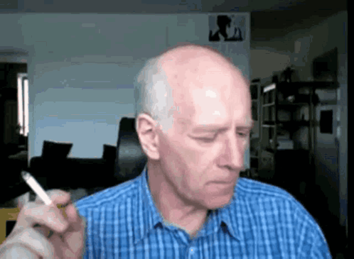 A Bald Man Is Smoking A Cigarette In A Blue Plaid Shirt GIF