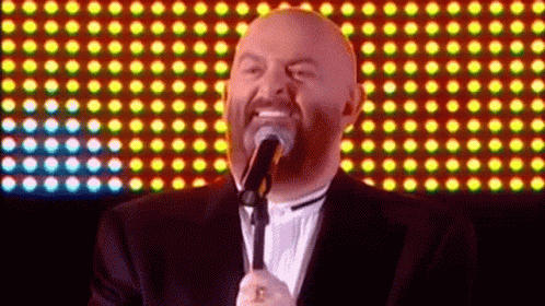 a bald man singing into a microphone with a beard