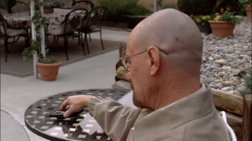 A Bald Man Sits At A Table With A Cell Phone GIF