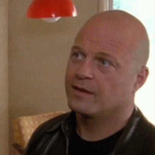A Bald Man Wearing A Black Shirt And A Black Leather Jacket Is Looking Up At Something . GIF