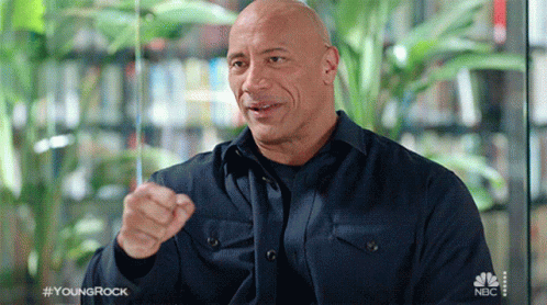 A Bald Man Wearing A Blue Shirt Is Pointing At The Camera . GIF