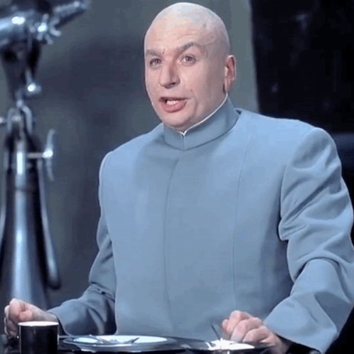 A Bald Man Wearing A Blue Suit Is Sitting At A Table GIF