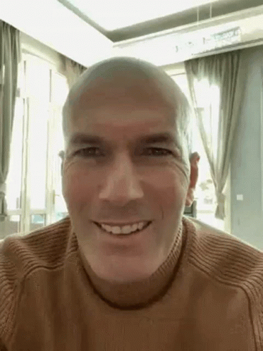 A Bald Man Wearing A Brown Sweater Is Smiling . GIF