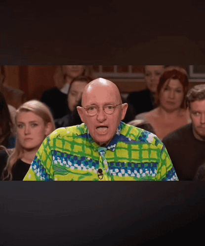 A Bald Man Wearing A Colorful Shirt And Tie Stands In Front Of A Crowd Of People GIF