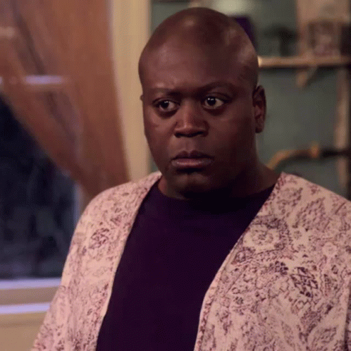 A Bald Man Wearing A Purple Shirt And A White Jacket Looks At The Camera . GIF