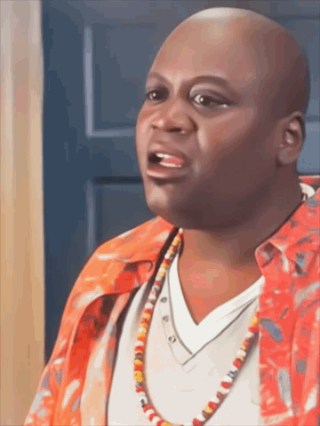 A Bald Man Wearing A Red Shirt And A Necklace Is Talking GIF