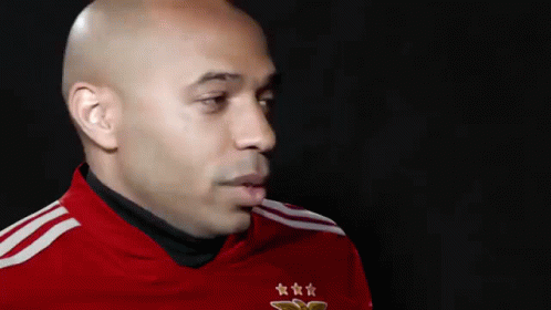A Bald Man Wearing A Red Shirt With Three Stars On It Is Looking At The Camera . GIF