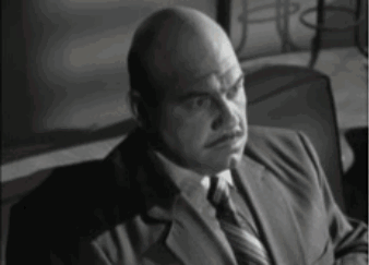 A Bald Man Wearing A Suit And Tie Is Sitting In A Chair GIF