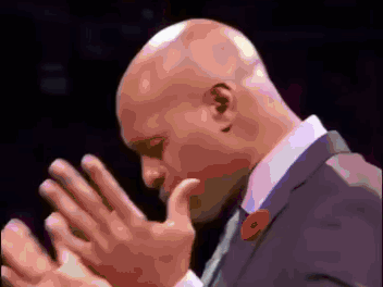 A Bald Man Wearing A Suit And Tie With A Red Poppy On His Lapel GIF