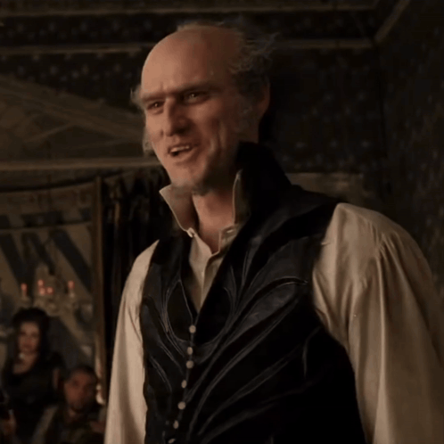 A Bald Man Wearing A Vest And A White Shirt Is Smiling GIF