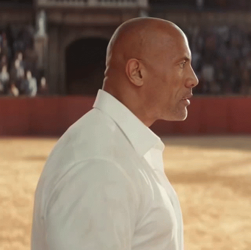 A Bald Man Wearing A White Shirt Stands In A Field GIF