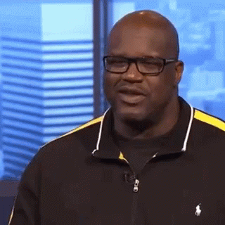 A Bald Man Wearing Glasses And A Black And Yellow Polo Shirt Is Standing In Front Of A Window . GIF