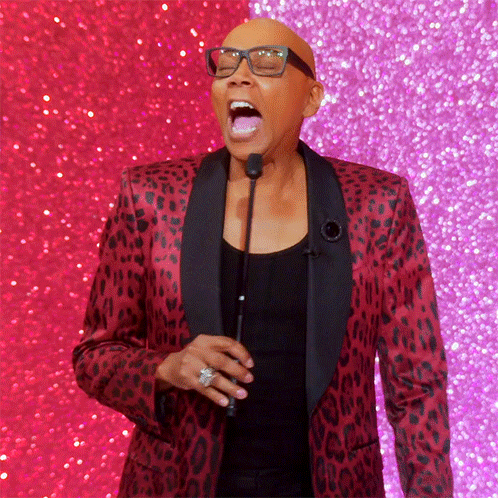 a bald man wearing glasses and a red leopard print jacket is speaking into a microphone