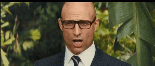 A Bald Man Wearing Glasses And A Suit And Tie Is Making A Funny Face . GIF