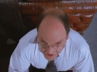 A Bald Man Wearing Glasses And A White Shirt And Tie Is Looking Up At The Camera . GIF