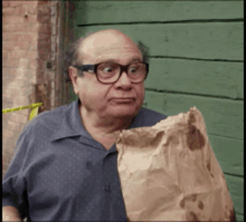 A Bald Man Wearing Glasses Is Holding A Brown Bag GIF